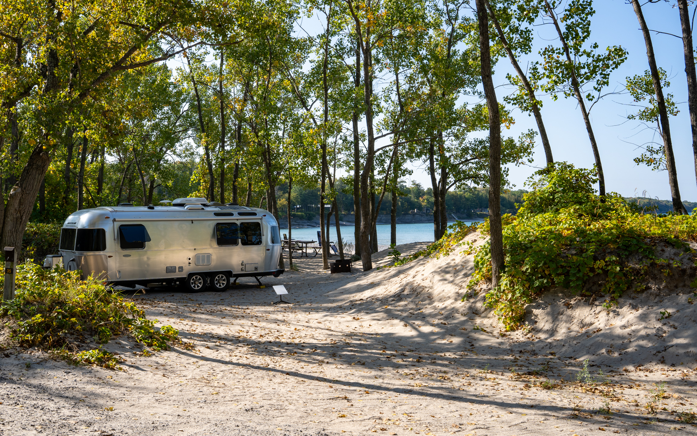 a silver camper parked on the sand with the beach in the background
