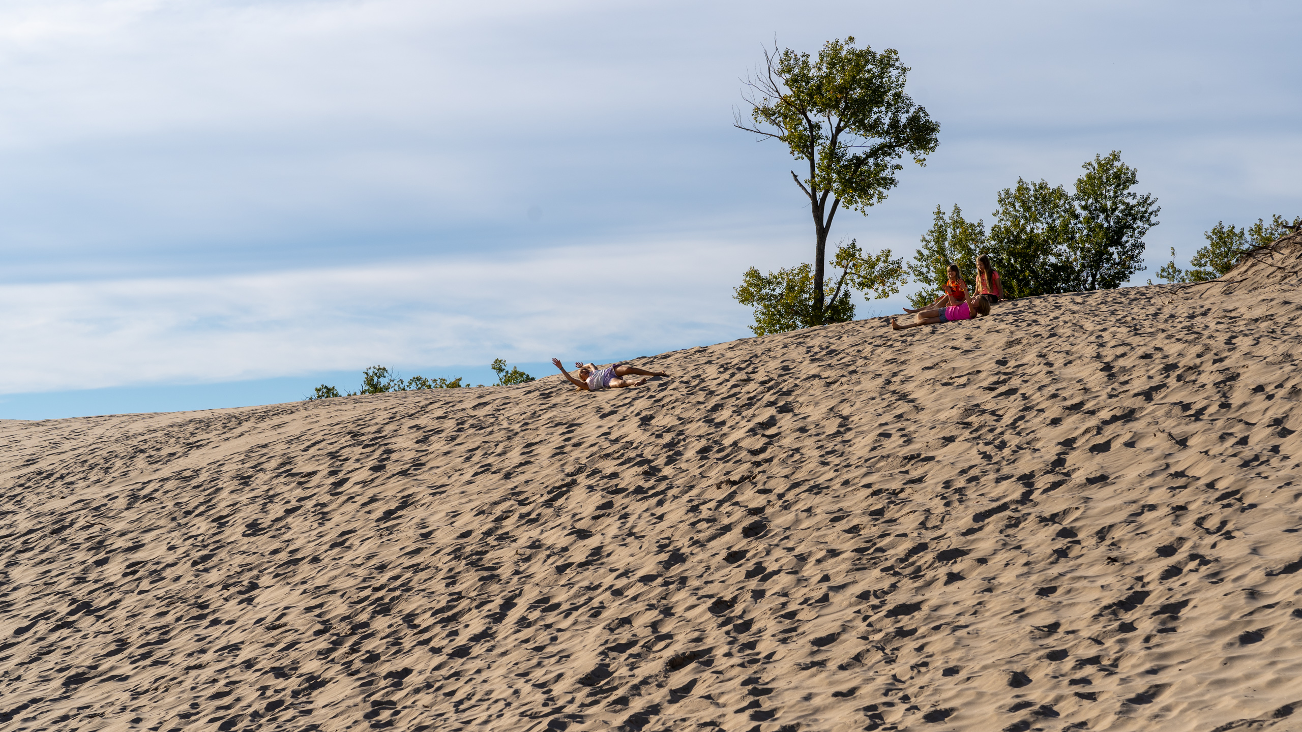 three kids wathcing another roll down the dunes at sandbanks provincial park